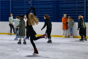 na zdjęciu lodowisko i osoby jeżdżące na nim, na środku tańcząca dziewczyna na łyżwach