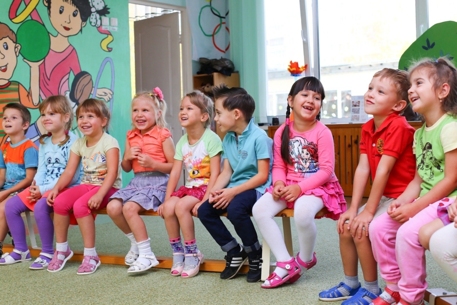 na zdjęciu znajdują się przedszkolaki siedzące na ławce i uśmiechające się
